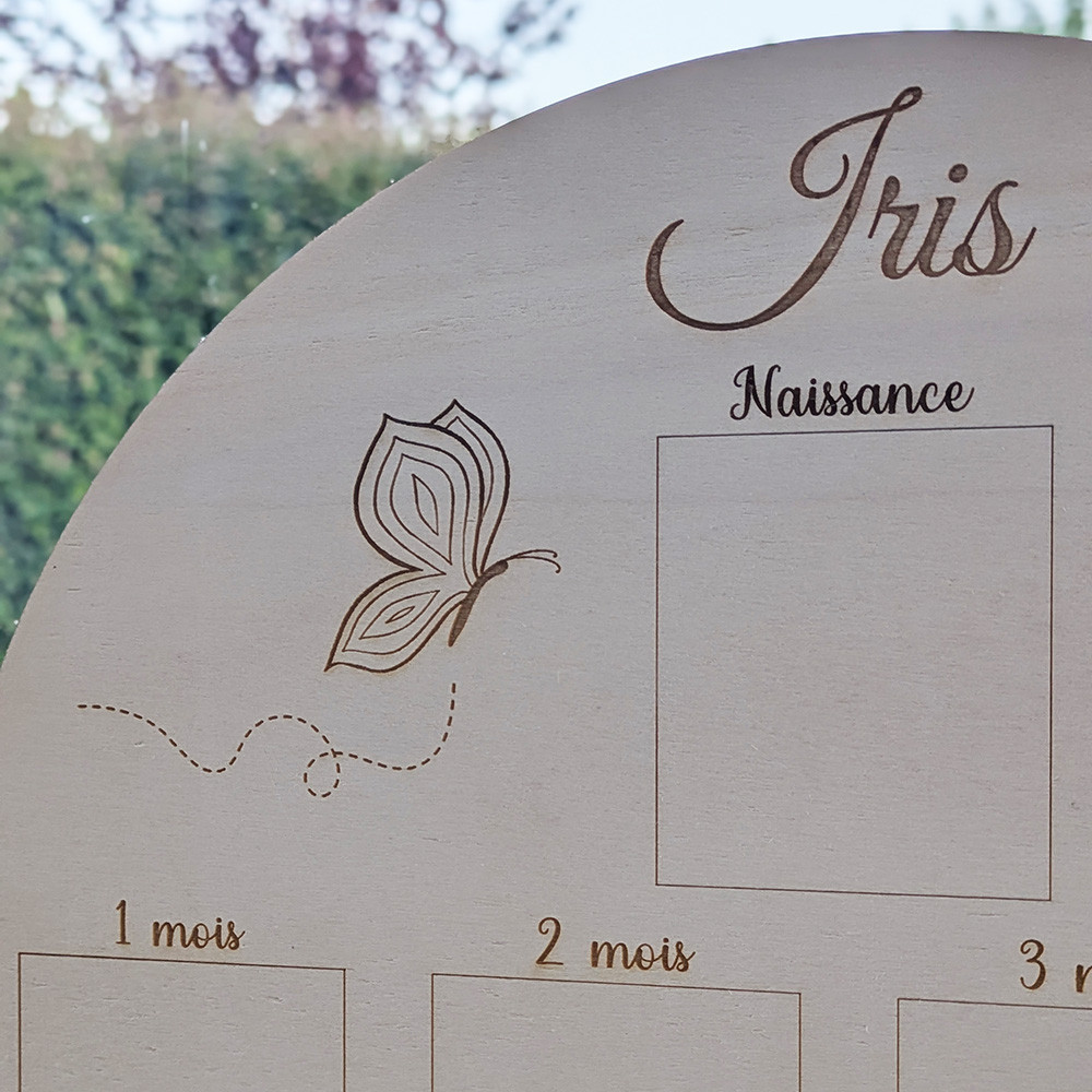 Gros plan sur la gravure du prénom et de l'illustration sur l'affiche de naissance en bois, avec les mentions 1 mois et 2 mois